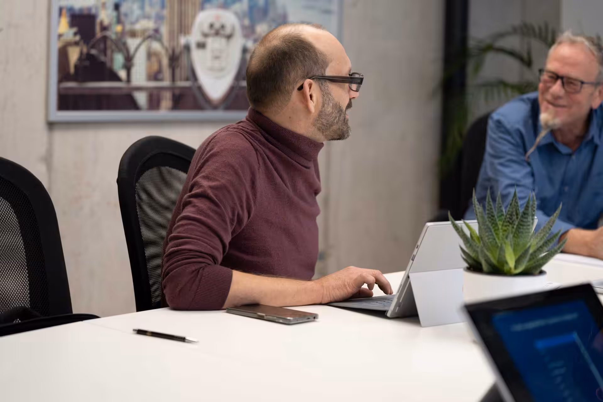 Ein Mann befindet sich in einem Meeting, arbeitet am Laptop und unterhält sich mit Kollegen über die neue Website